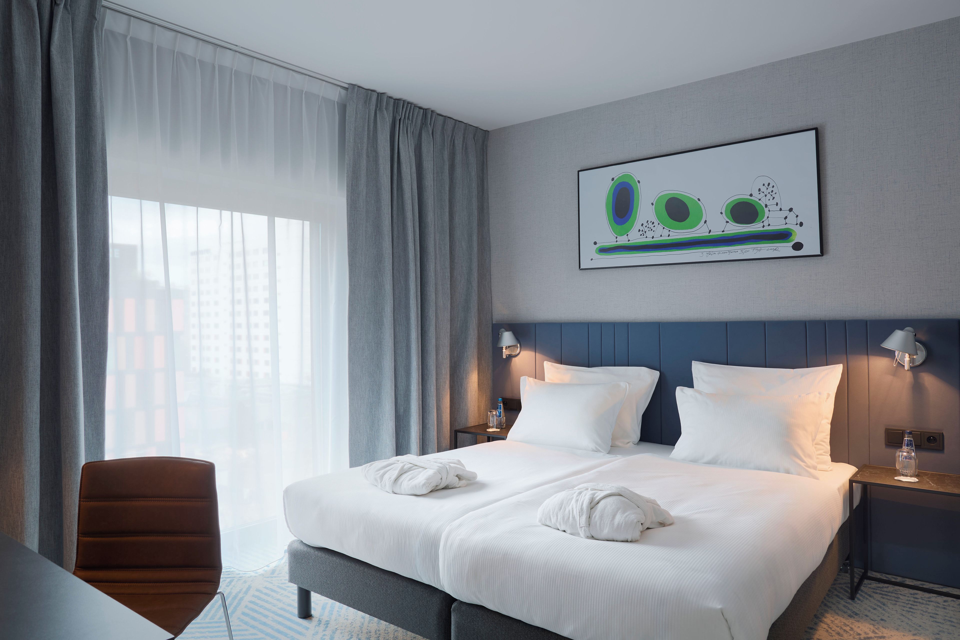 A hotel room with a large bed, two bedside tables, a chair, and a window with curtains.