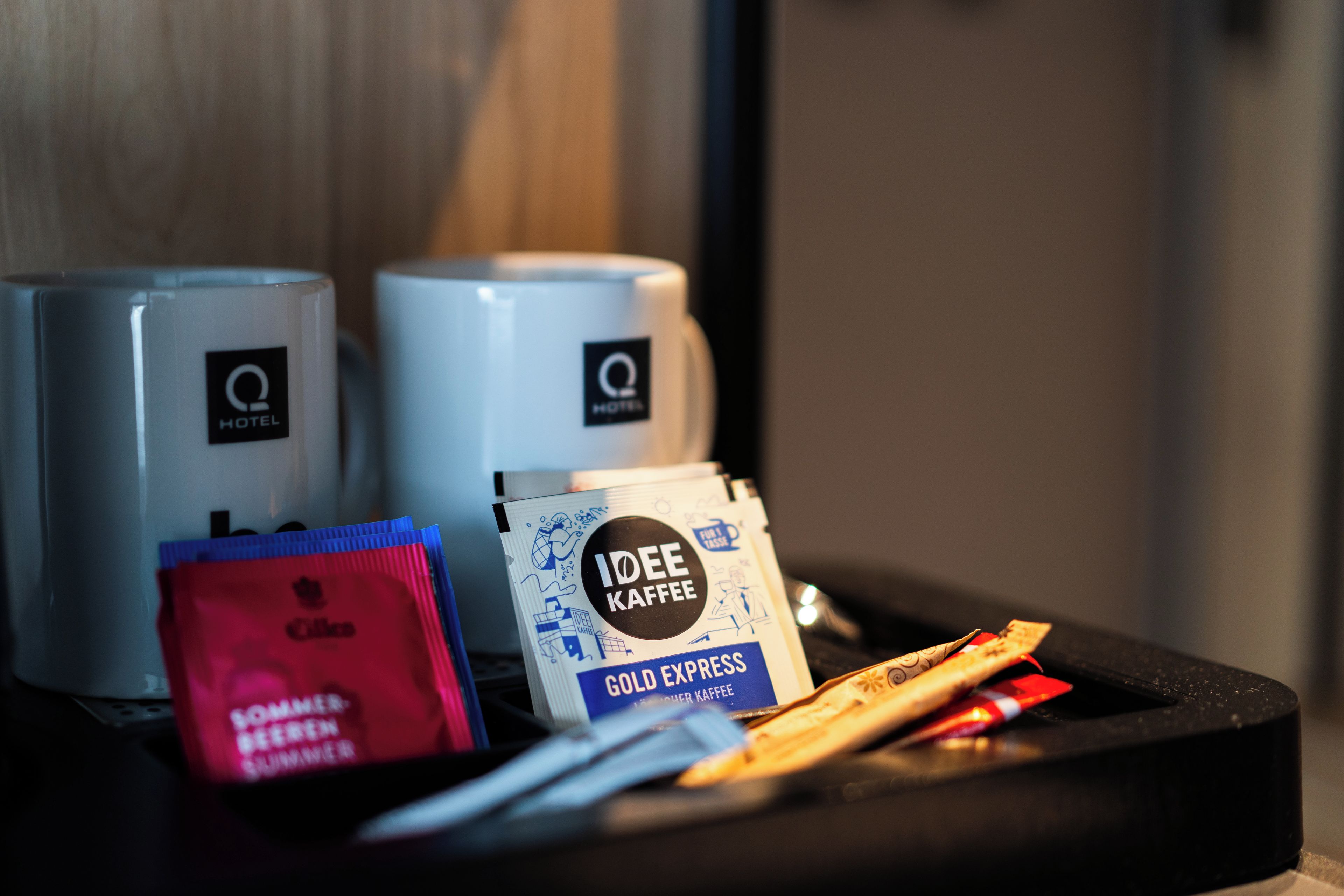 A tray with a coffee pod, a branded mug, and a red packet, likely containing a beverage or snack.