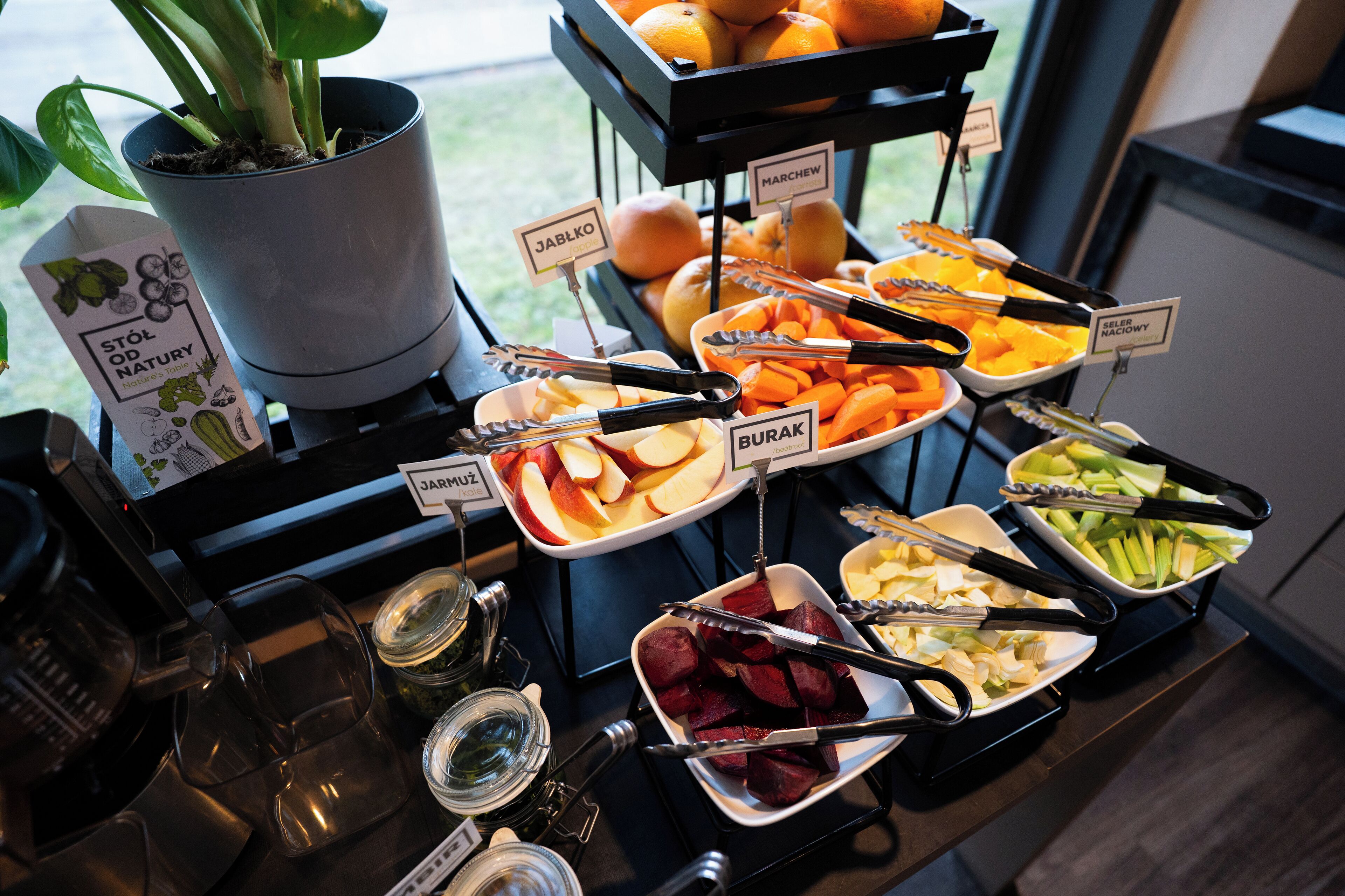 A buffet with various fruits and vegetables, including apples, oranges, and beets, arranged on a table with serving utensils.