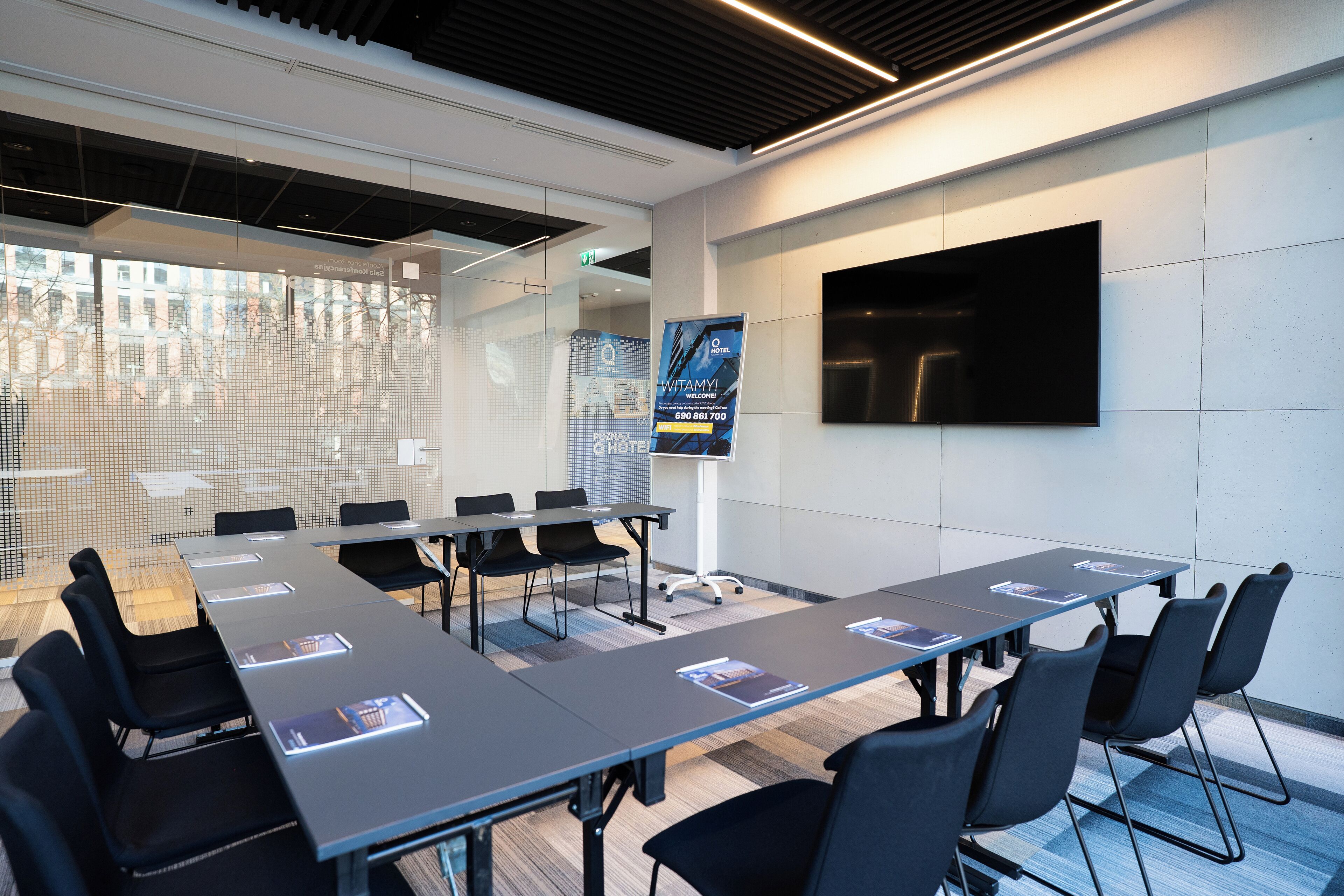 A modern conference room with a long table, black chairs, and a large screen.
