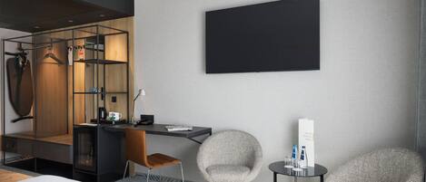 Una habitación de hotel moderna con una cama, un escritorio, dos sillas, un televisor y un espejo.