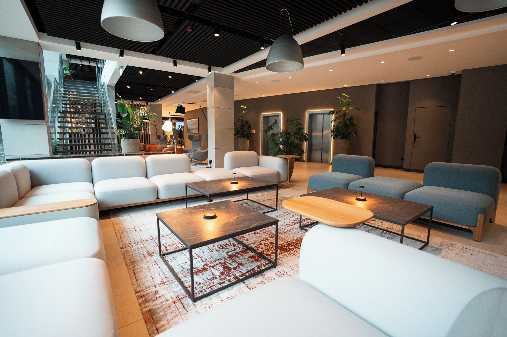A modern lobby with a staircase, seating areas, and a reception desk.