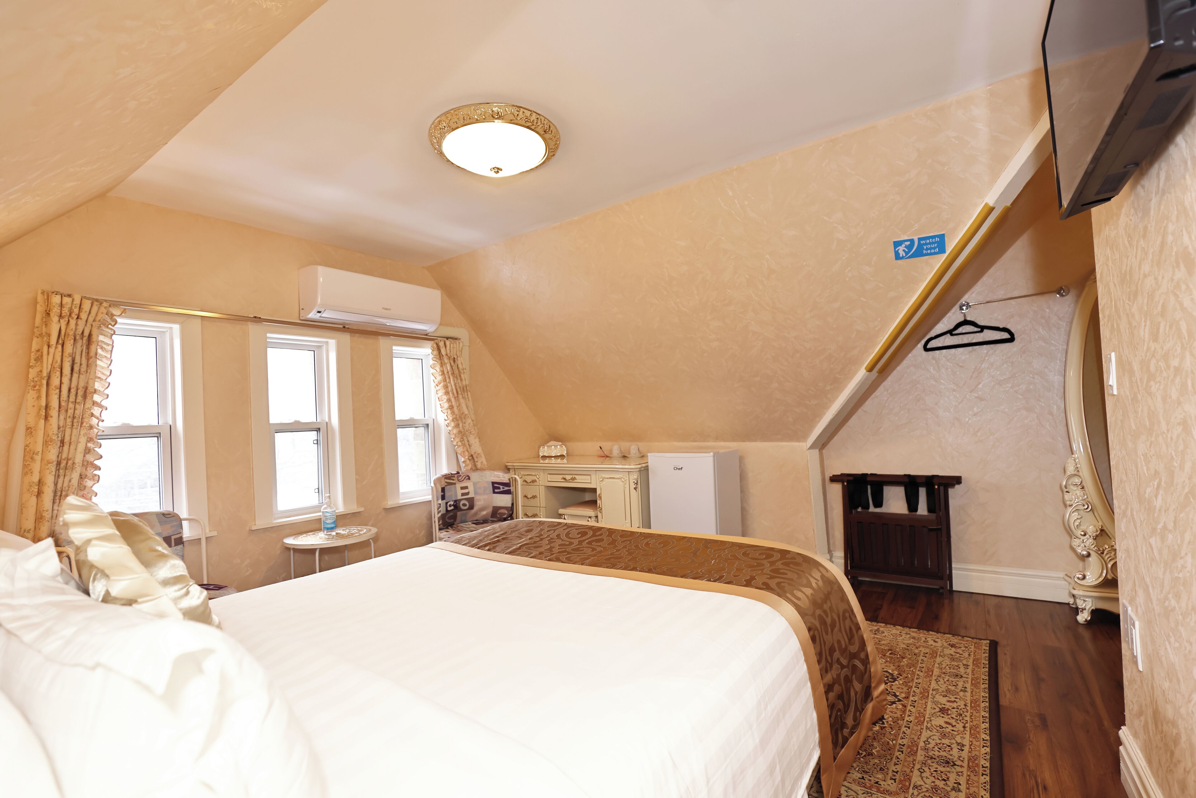 A hotel room with a large bed, a desk, a wardrobe, and a television.