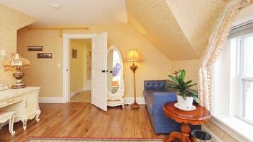 A room with a wooden floor, a blue sofa, a white dresser, a mirror, a lamp, and a potted plant.