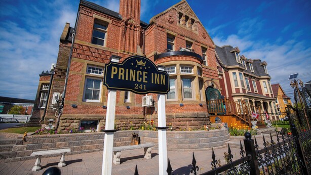 A brick building with a sign reading "Prince Inn 241" and a stone bench in front.