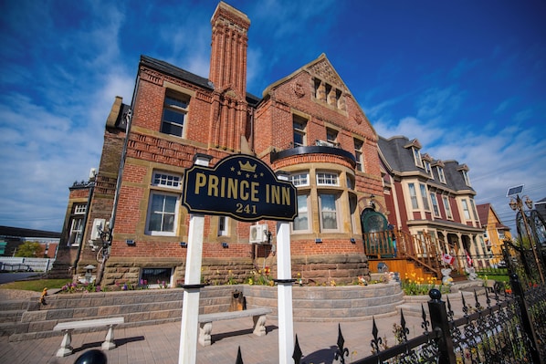 A brick building with a sign reading "Prince Inn 241" and a stone bench in front.