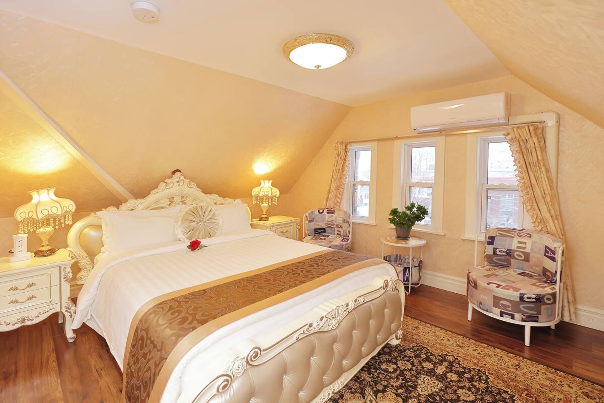 A bedroom with a large bed, bedside lamps, a small table with a plant, and a chair.