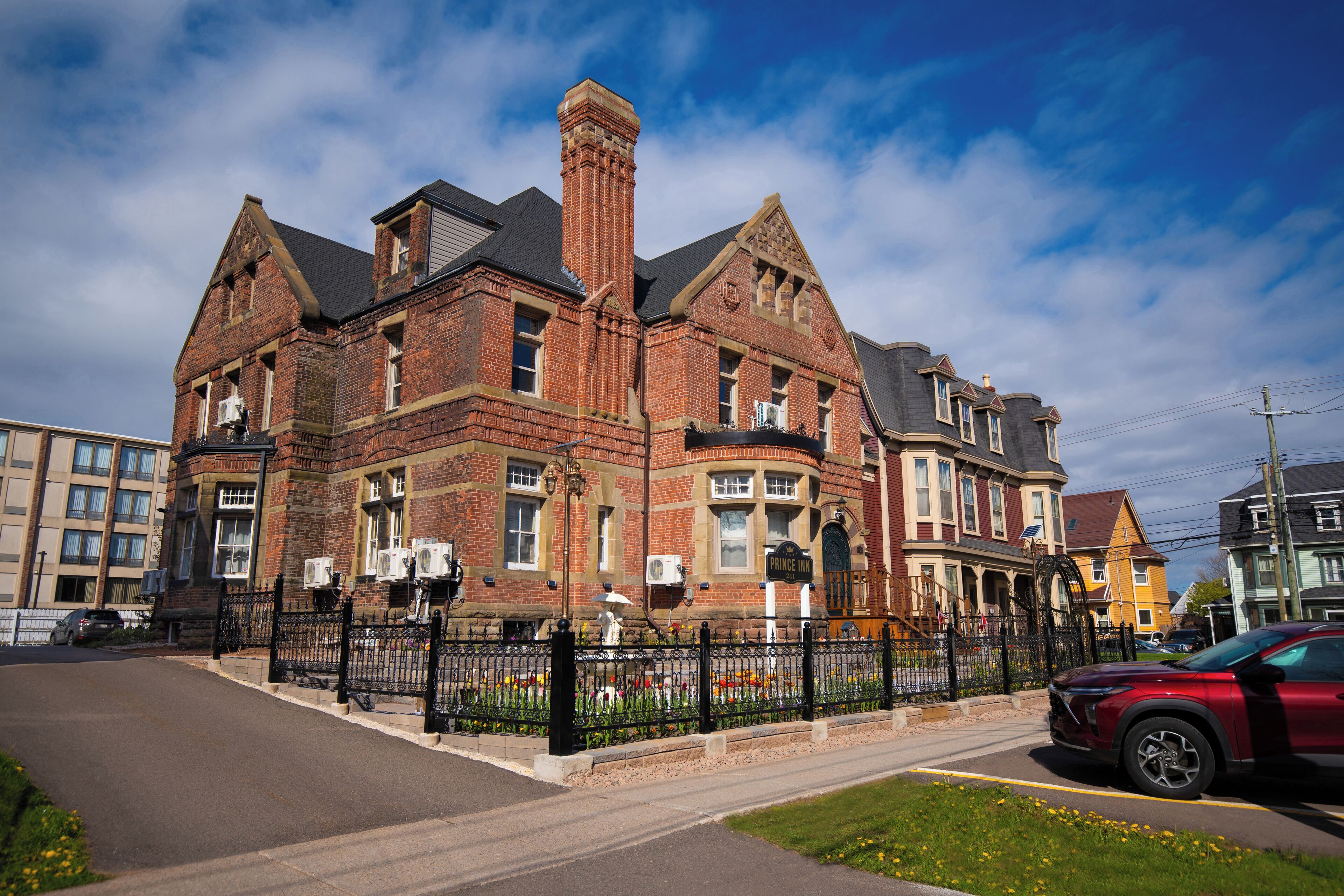 A historic brick building with a prominent chimney, large windows, and a black iron fence.