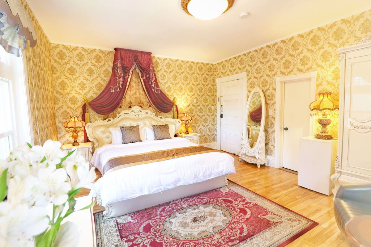 A bedroom with a large bed, a red and white patterned rug, and a mirror on the wall.