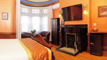 A hotel room with a large bed, a fireplace, a television, and a desk.