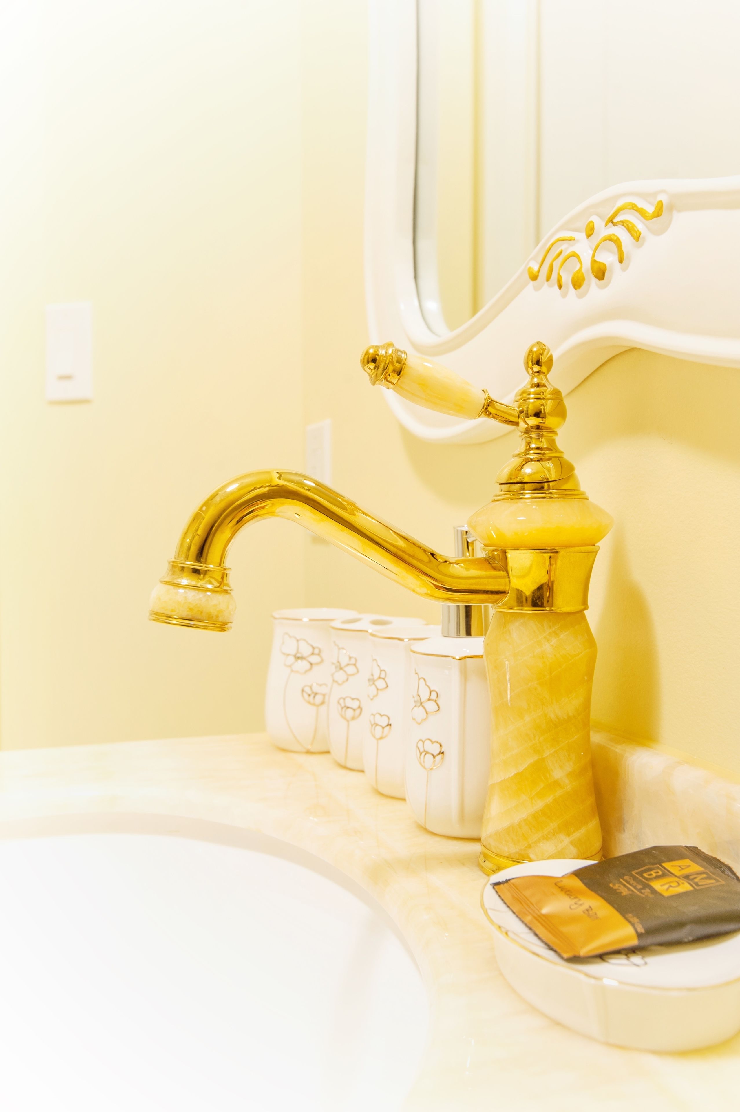 A bathroom with a gold faucet, a mirror, and a tissue box.