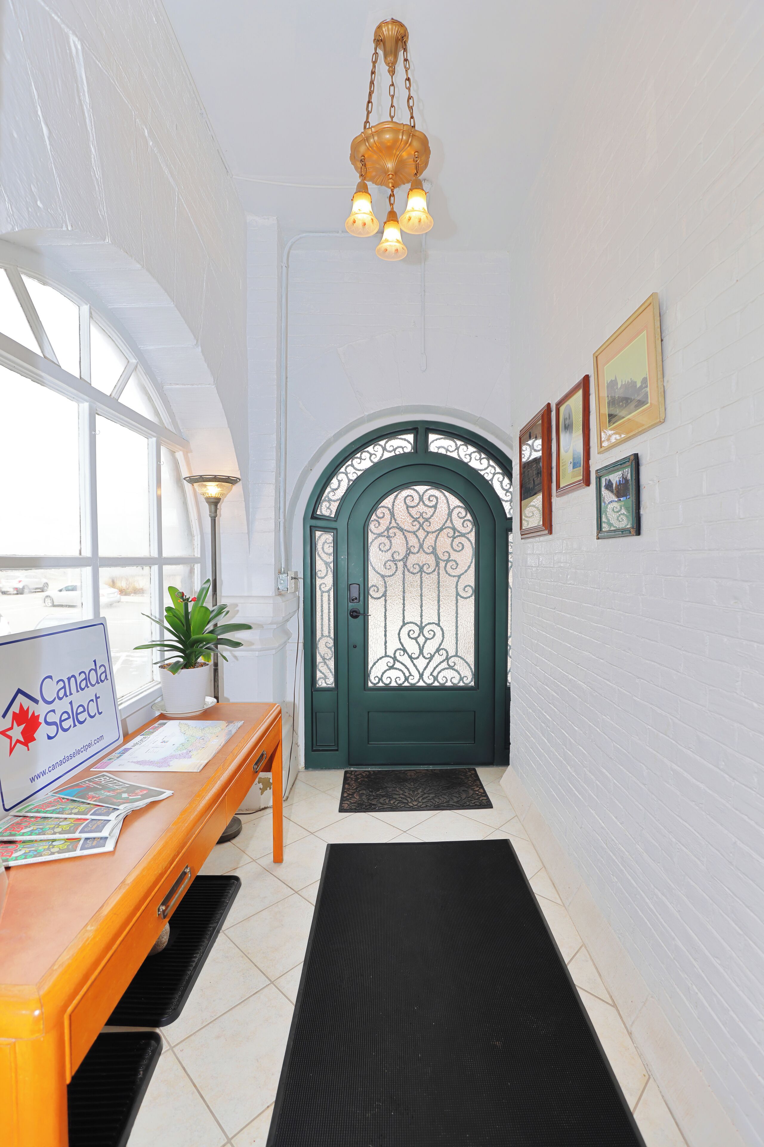 A reception area with a Canada Select sign, a desk with brochures, a potted plant, a green door with decorative glass, and framed pictures on the wall.