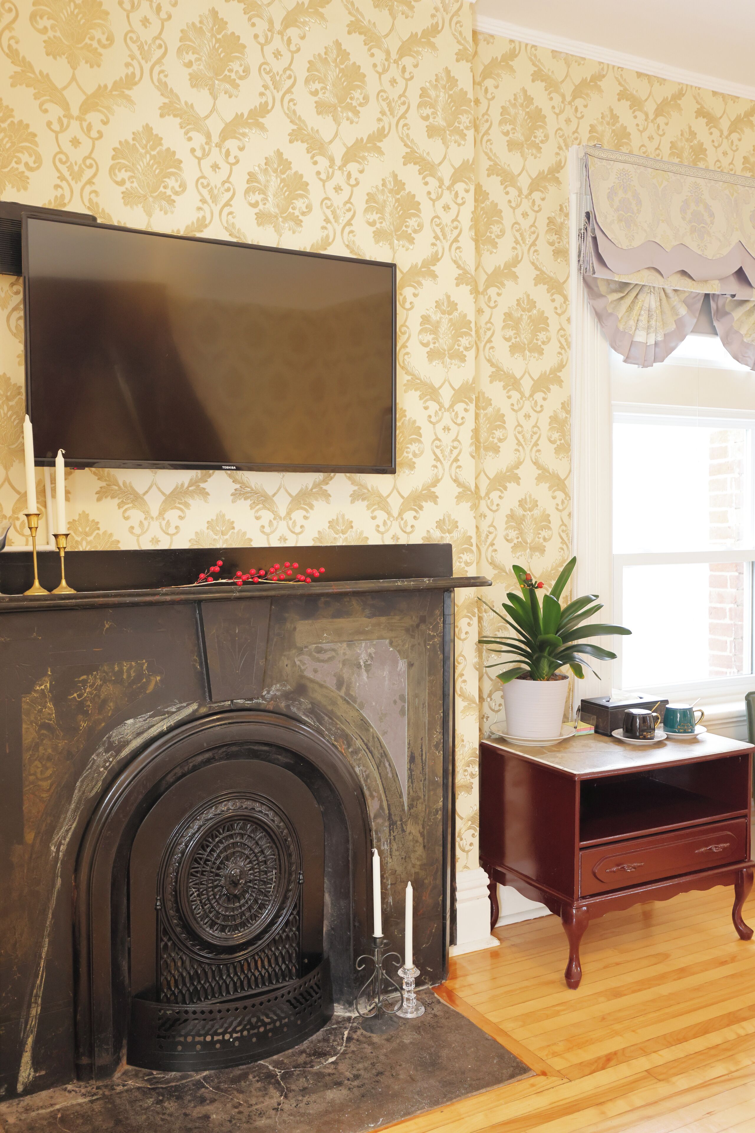 Un salón con chimenea, un televisor montado encima y una planta en una mesita.