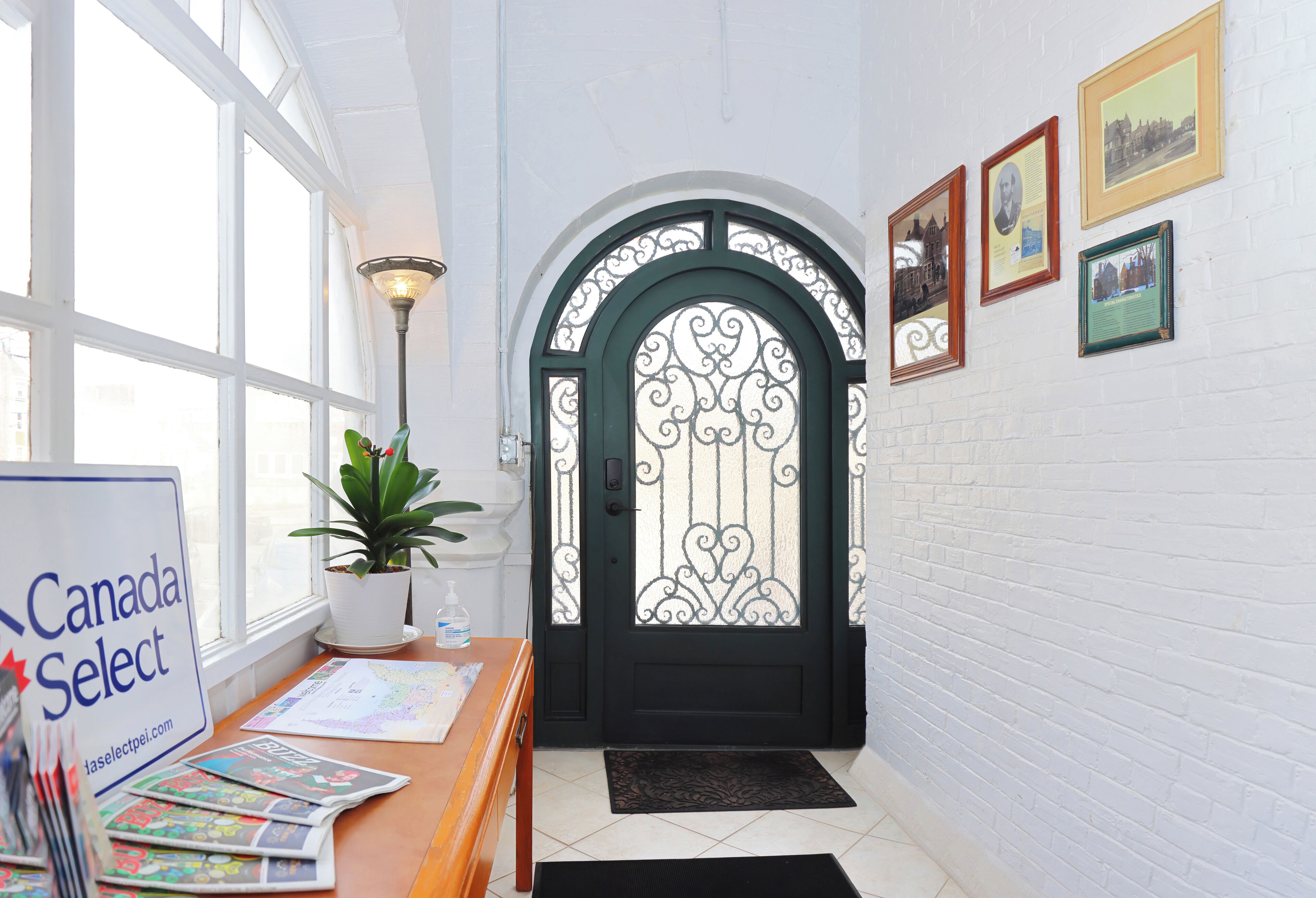 A reception area with a black door, a potted plant, a sign reading "Canada Select," and framed pictures on the wall.
