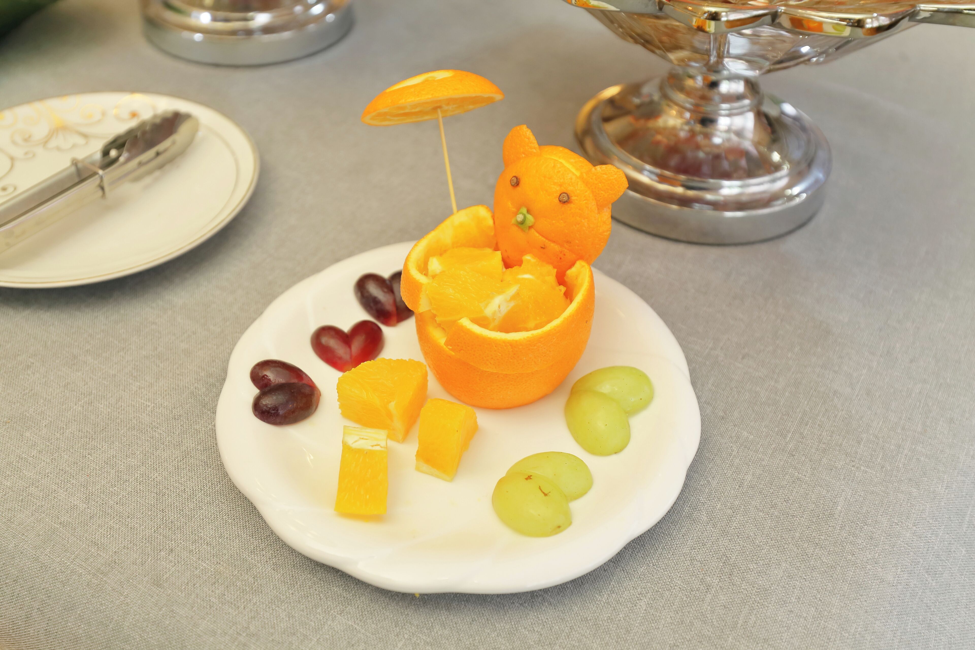 Ein Teller mit einer Bärenform aus Obst, darunter Trauben, eine Orange und eine Zitrone.