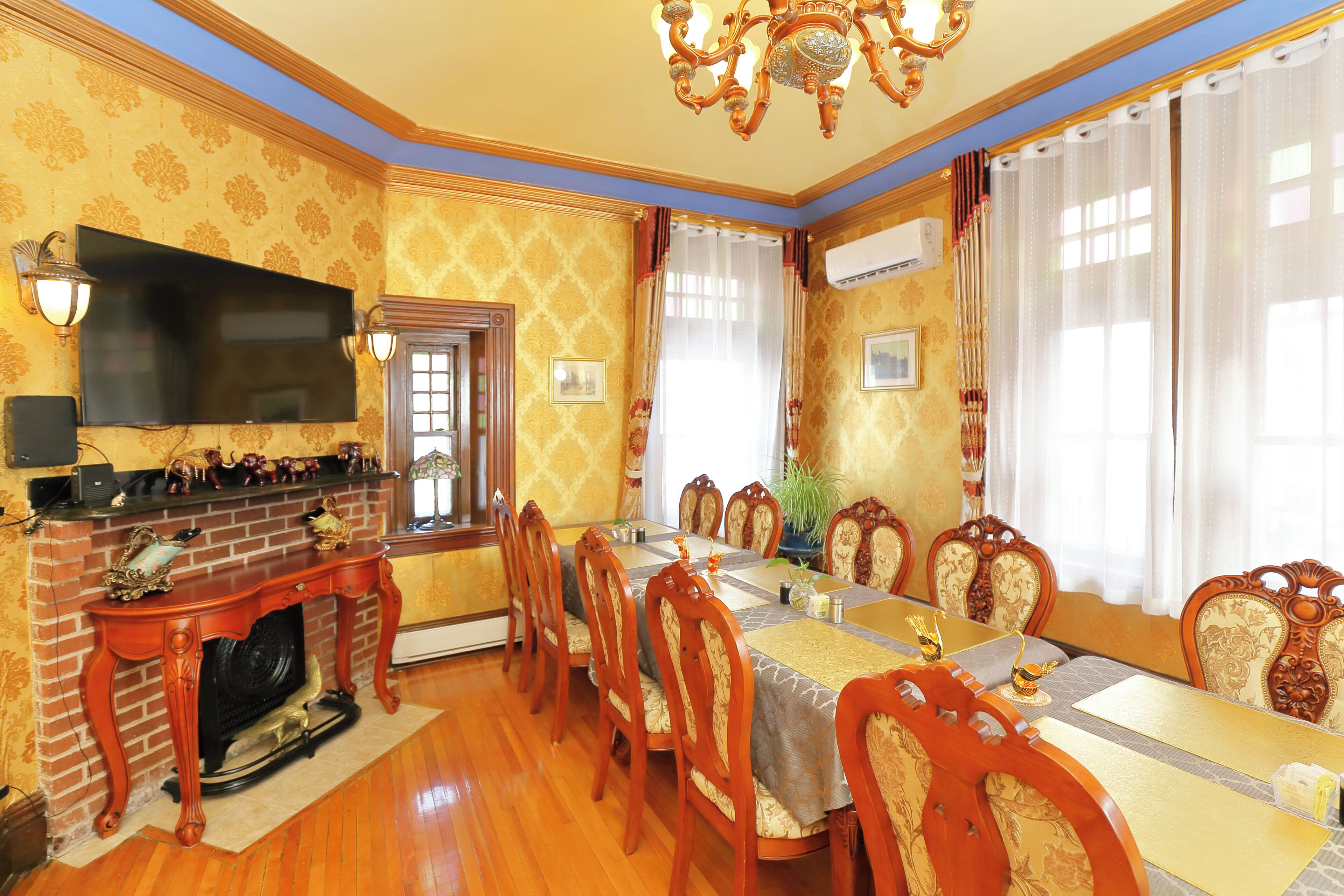 Comedor con chimenea de ladrillo, televisor de pantalla plana montado arriba y una gran mesa de comedor rodeada de sillas ornamentadas.