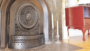 A fireplace with intricate metalwork, a white candle, and a red cabinet with a plant.