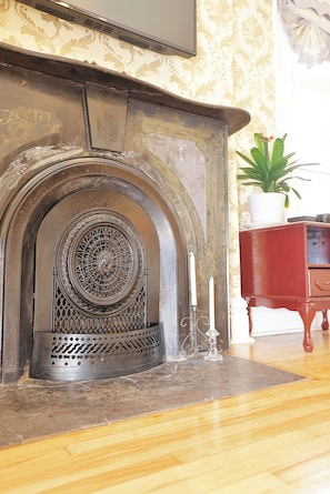 A fireplace with intricate metalwork, a white candle, and a red cabinet with a plant.