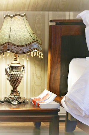 A wooden nightstand with a green lamp, a book, and a white bed with a wooden headboard.