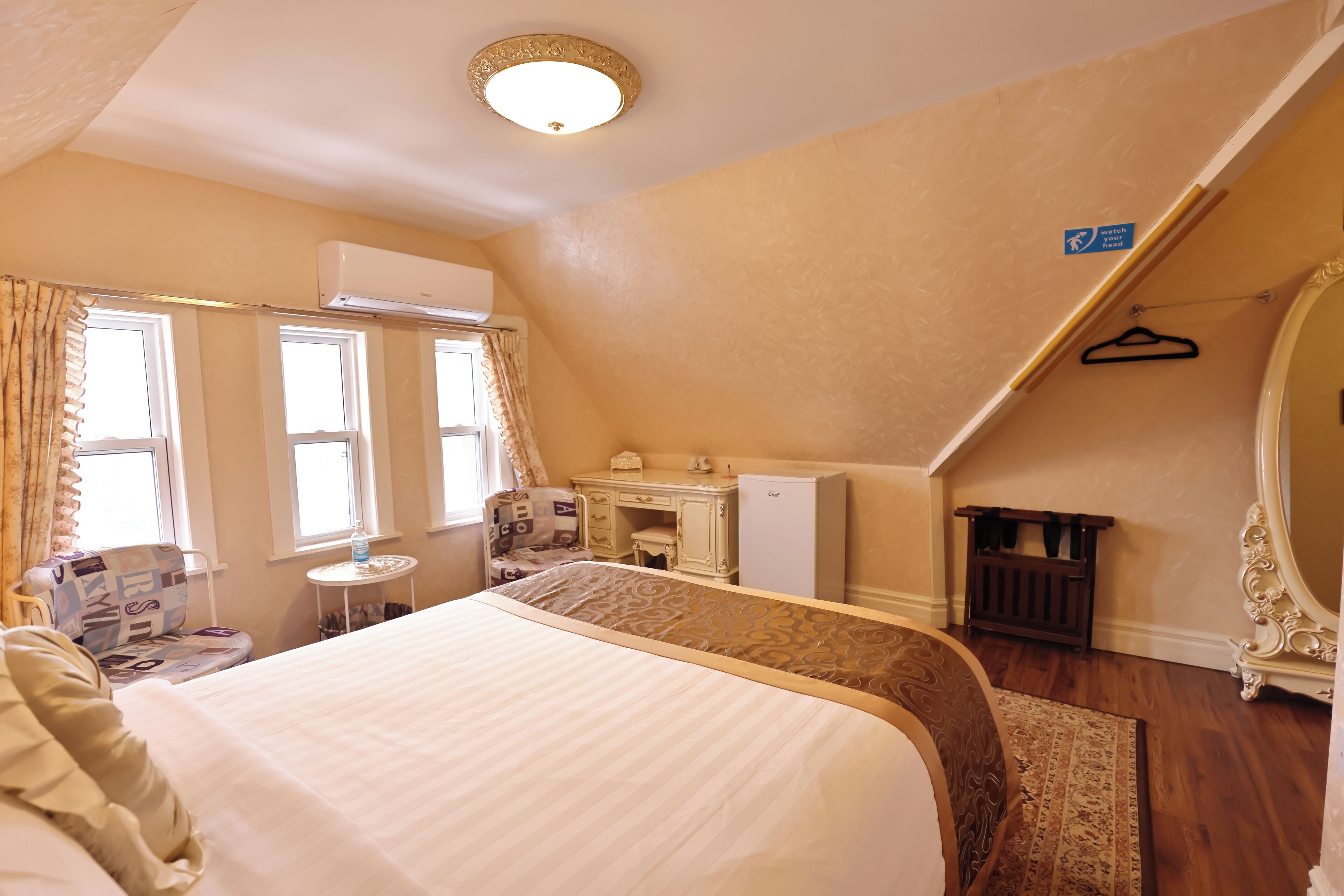 A bedroom with a large bed, a desk, an air conditioning unit, and a mirror.