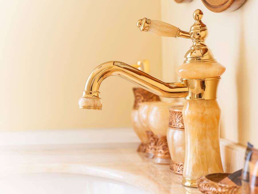 A bathroom with a gold faucet and a marble countertop.