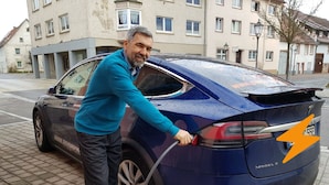 Un homme recharge une Tesla Model S sur une rue pavée de briques.