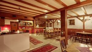 Un grand espace dédié à la salle à manger, avec des tables et des chaises en bois, une cuisine à l’arrière-plan et un coin bar.
