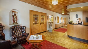 Un hall d’entrée avec un plafond en bois, un comptoir d’accueil, un fauteuil en cuir et une table recouverte d’un tapis rouge.