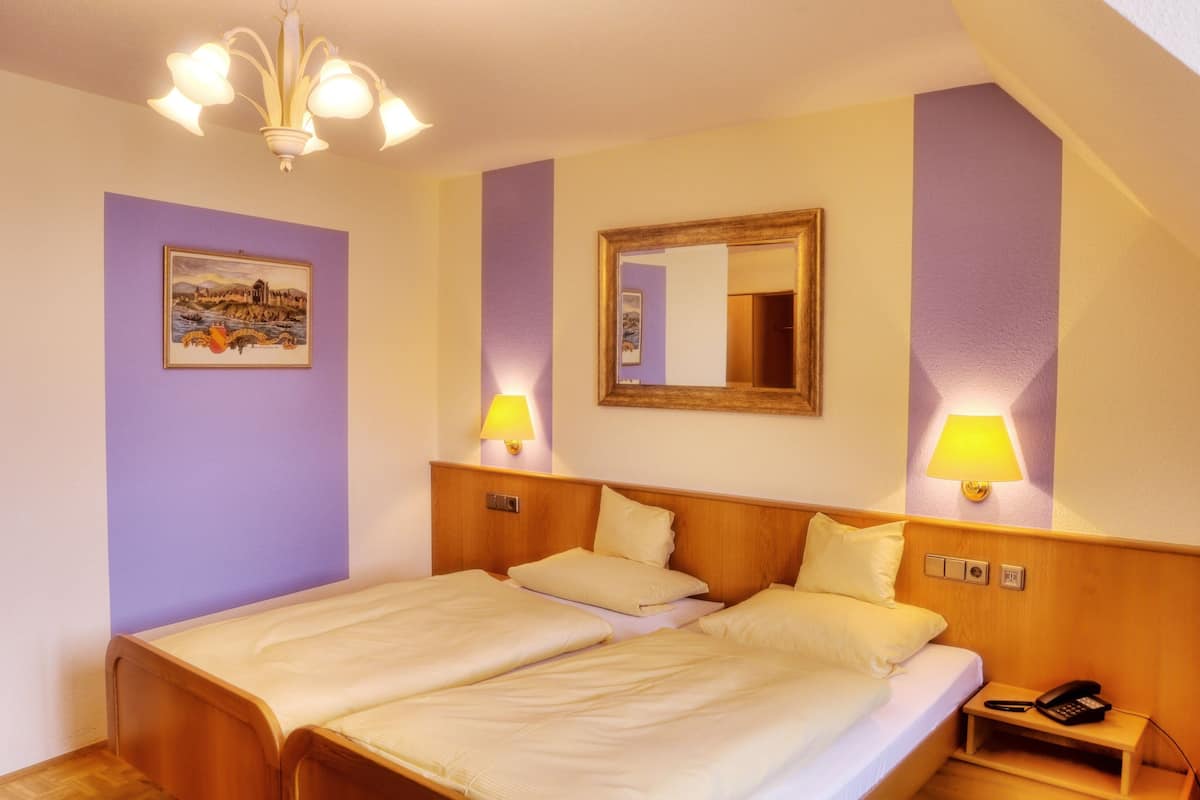 Habitación de hotel con dos camas, un cabecero de madera, una mesita de noche con teléfono y lámparas fijadas a la pared.