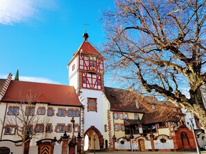 A traditional European building with a prominent tower, a large tree in the foreground, and a clear blue sky. - Hotel Restaurant Lindenhof (Braeunlingen)