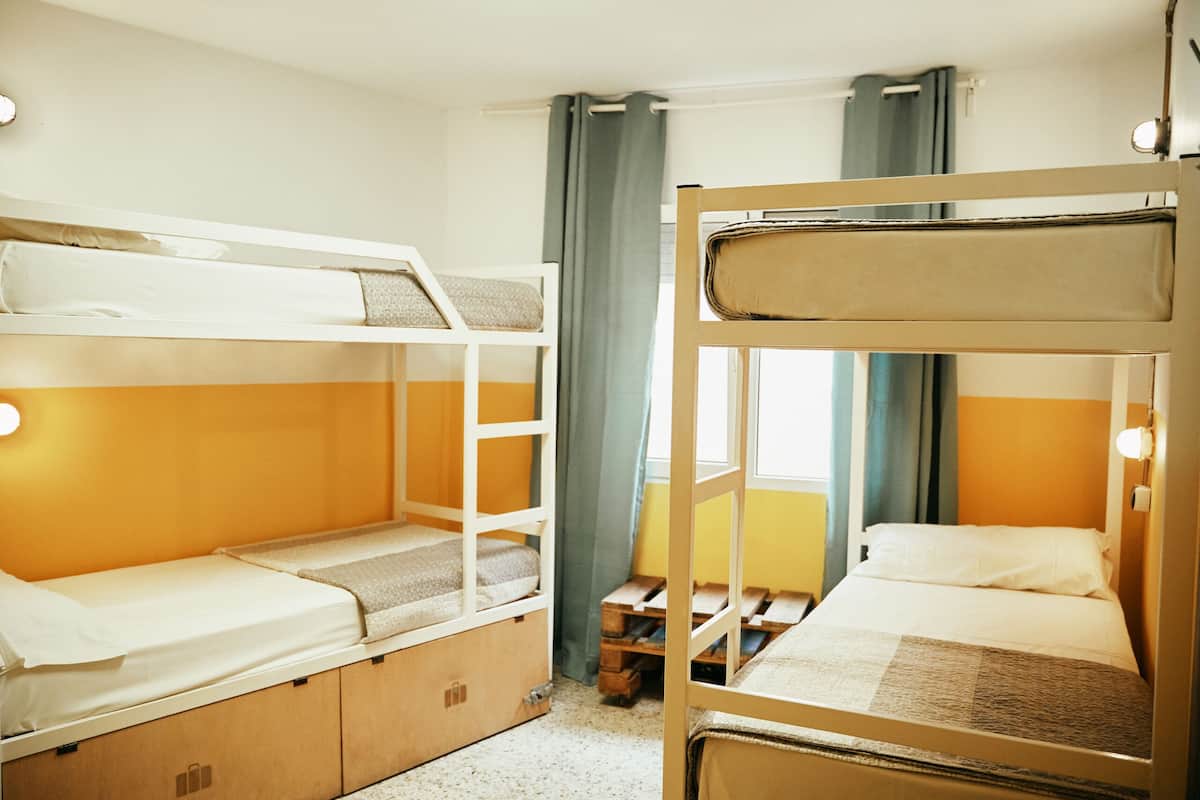 Een kamer met stapelbedden, houten opbergvakken en een raam met gordijnen.