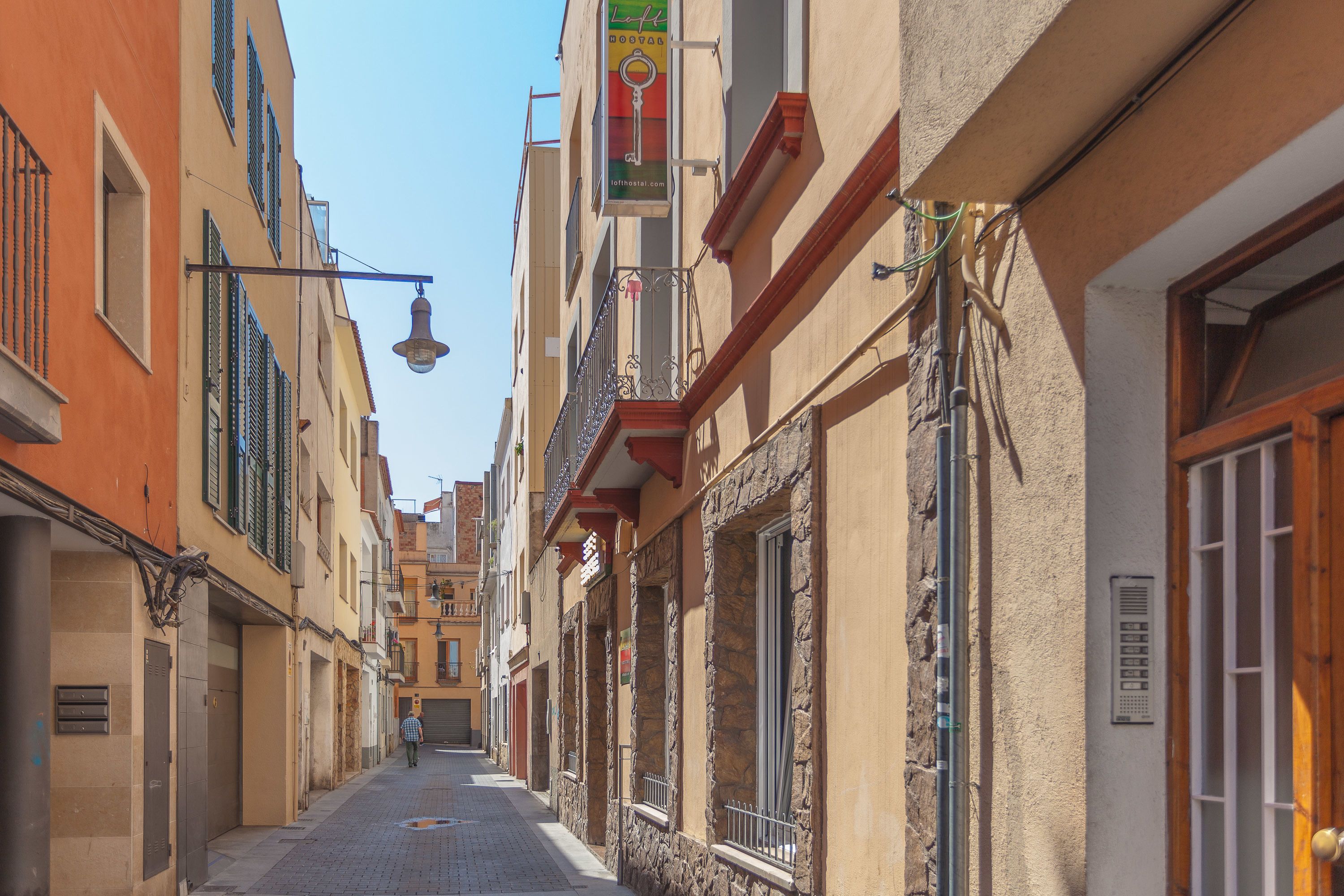 A narrow street with buildings on both sides, featuring balconies and a clear sky.