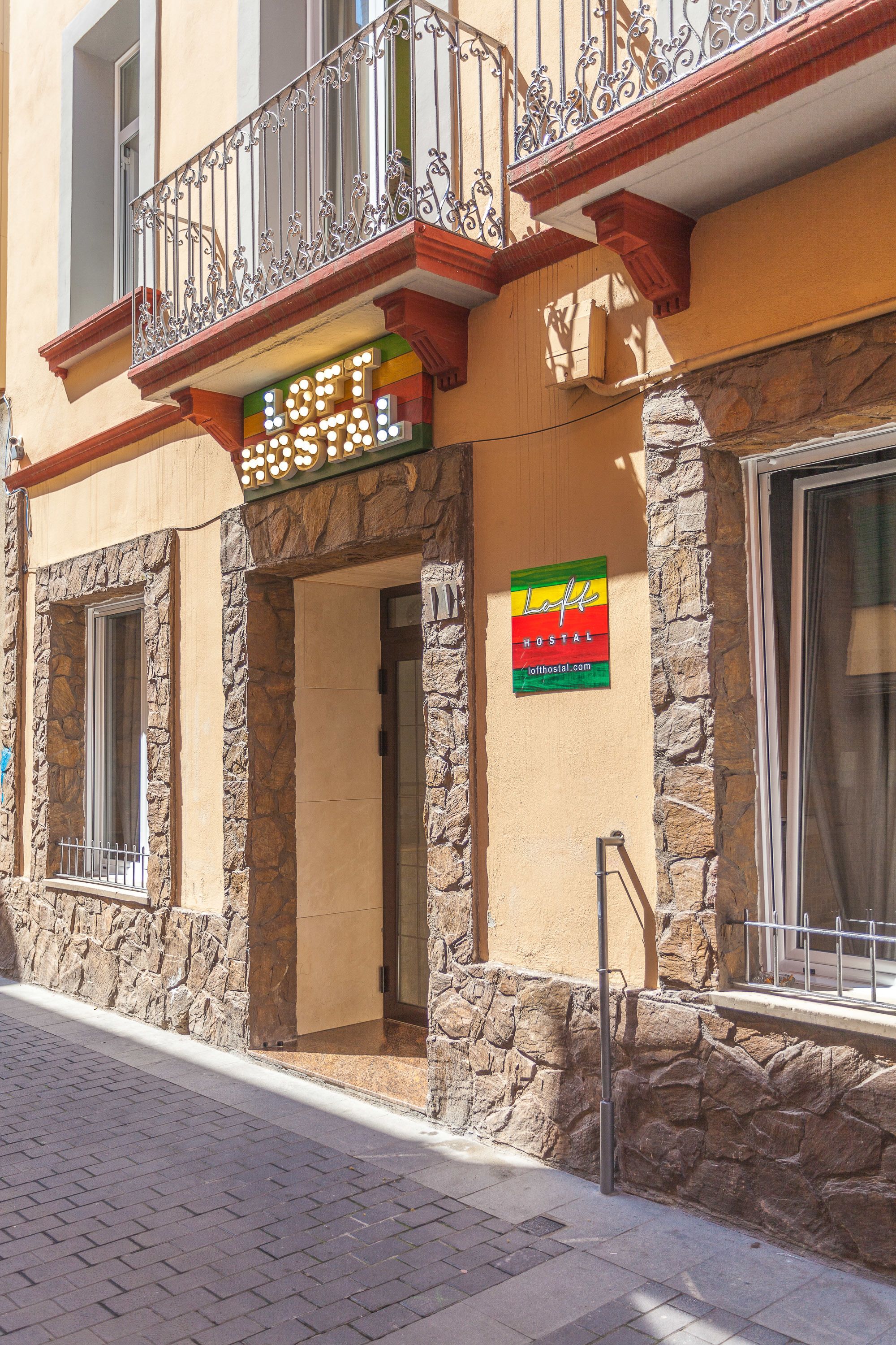 A hotel with a stone facade, a balcony with wrought iron railings, and a sign indicating it is a hostel.