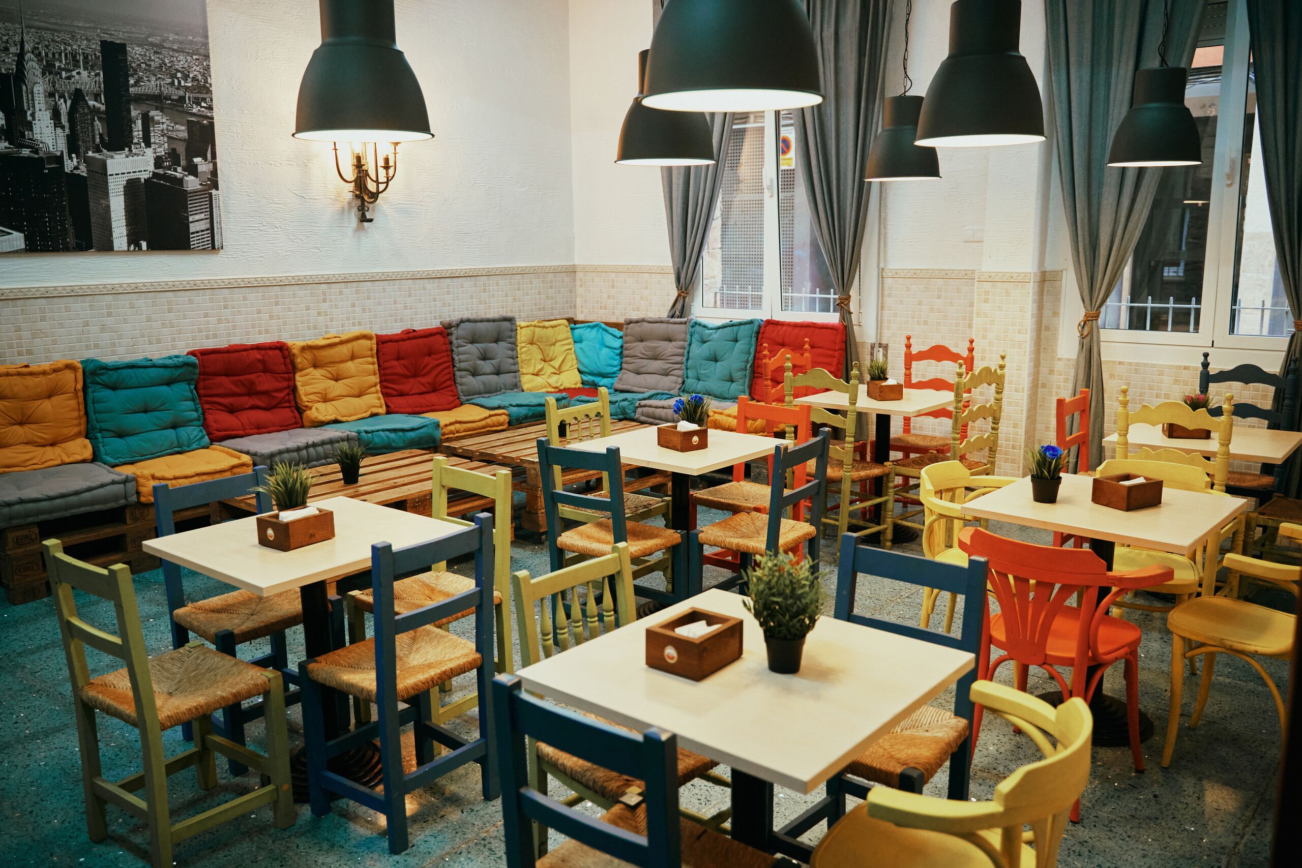 Un interior de restaurante con un sofá largo y colorido, varias mesas y sillas.