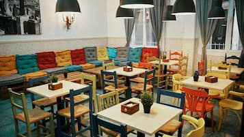 Un interior de restaurante con un sofá largo y colorido, varias mesas y sillas.
