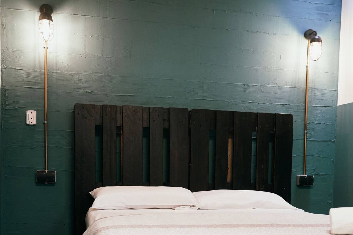 Een bed met een houten hoofdbord in een kamer met teal muren en twee wandlampen.