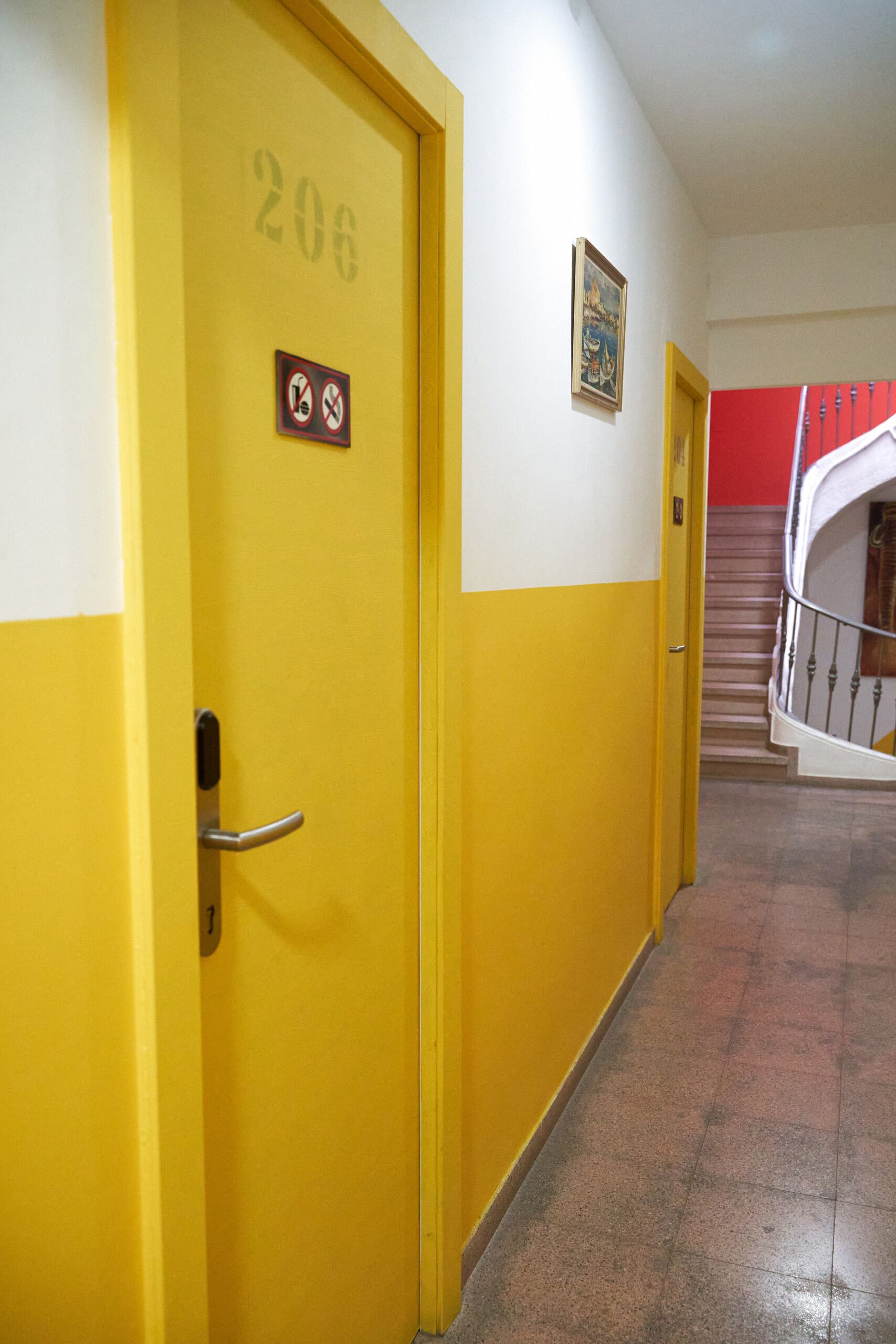 Une porte jaune portant le numéro 206, un panneau « interdiction de fumer » et un escalier avec un mur rouge en arrière-plan.