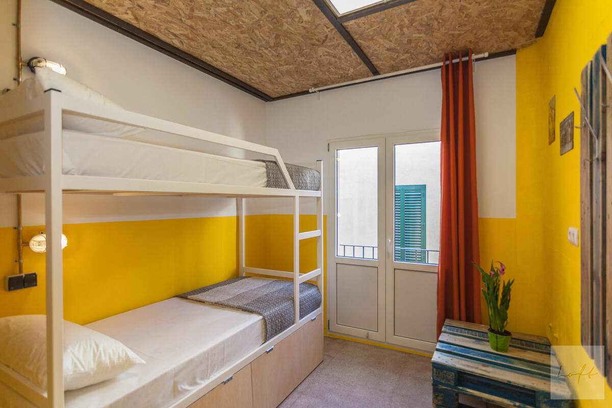 Een kamer met stapelbedden, een tafeltje met een plant en een raam met gordijnen.