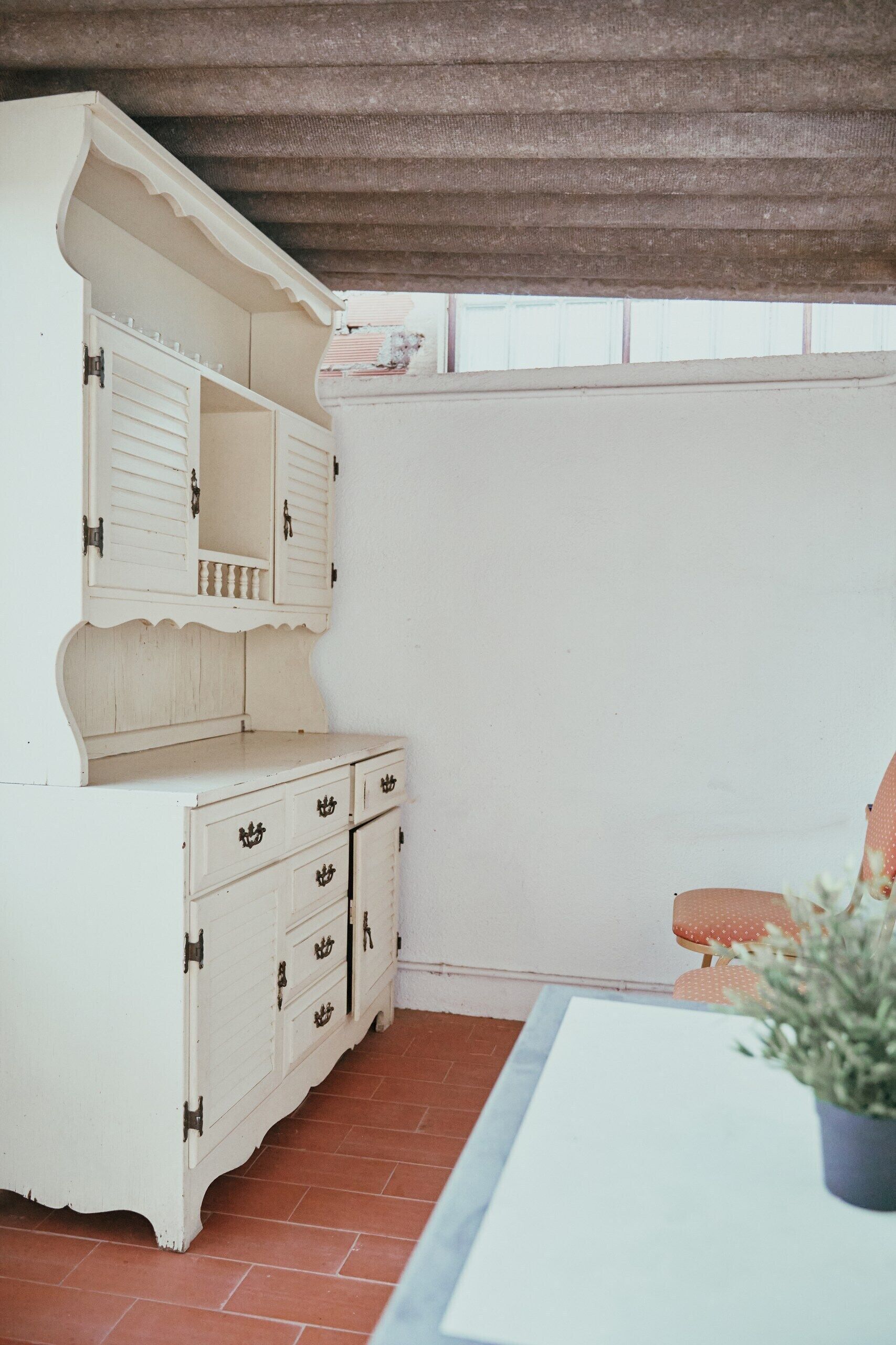 Un mueble blanco de madera con cajones y un estante, una mesa blanca y una planta en maceta.