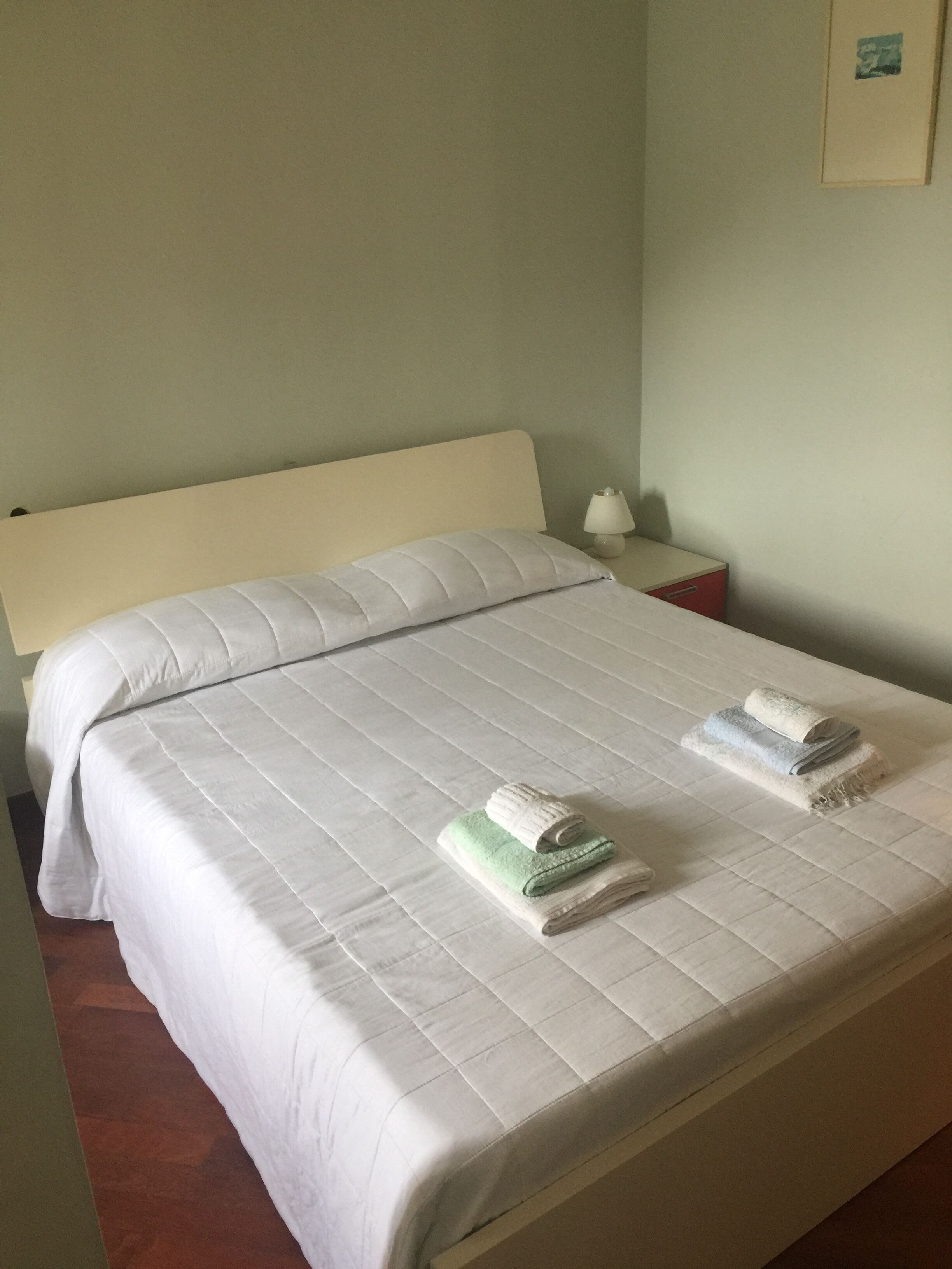 Una cama bien hecha con edredón blanco y dos toallas enrolladas.