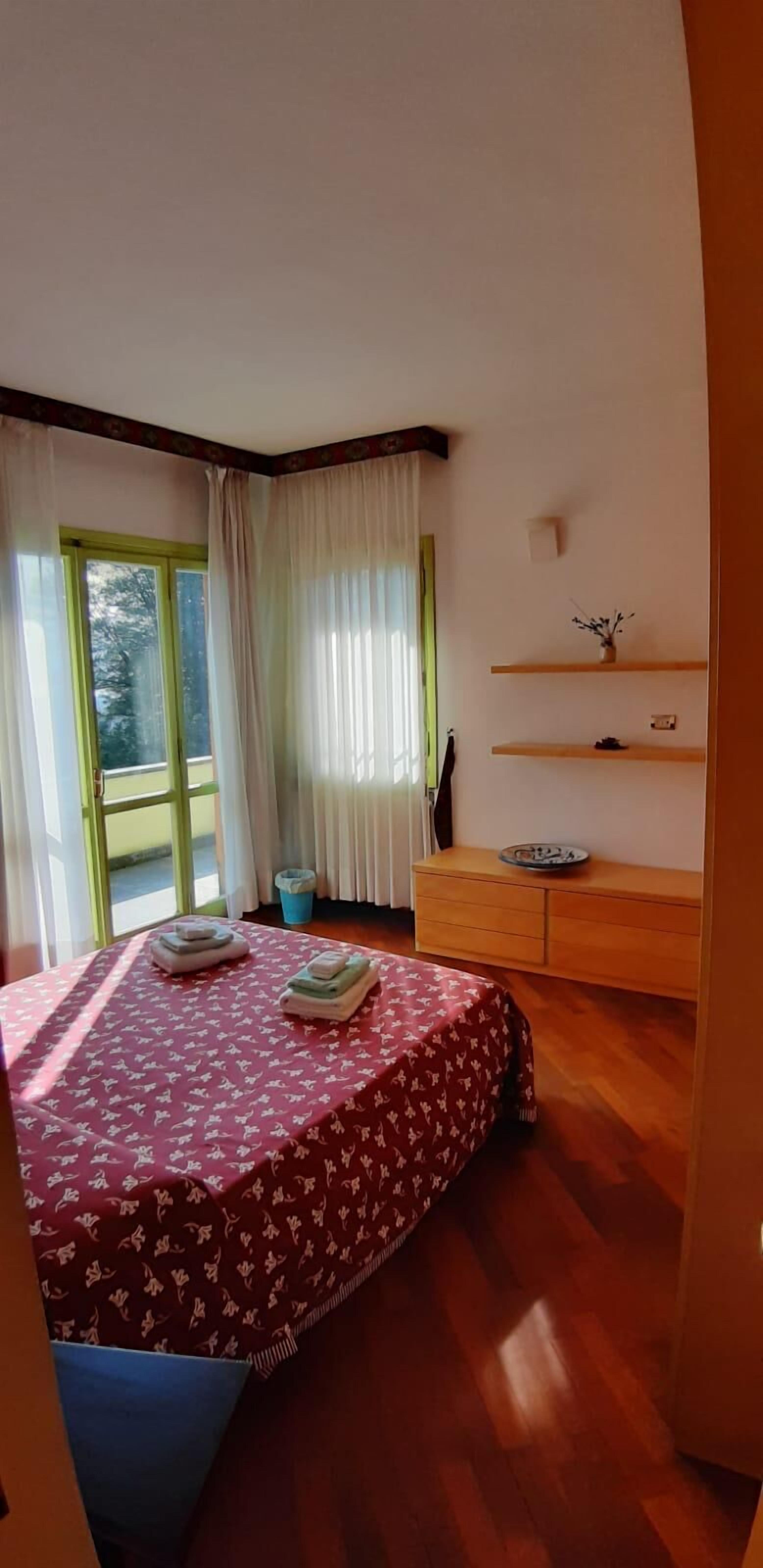 A bedroom with a bed, a wooden dresser, a window with curtains, and a view of the outdoors.