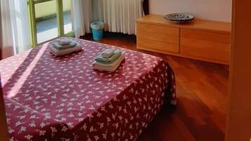 A bedroom with a bed, a wooden dresser, a window with curtains, and a view of the outdoors.
