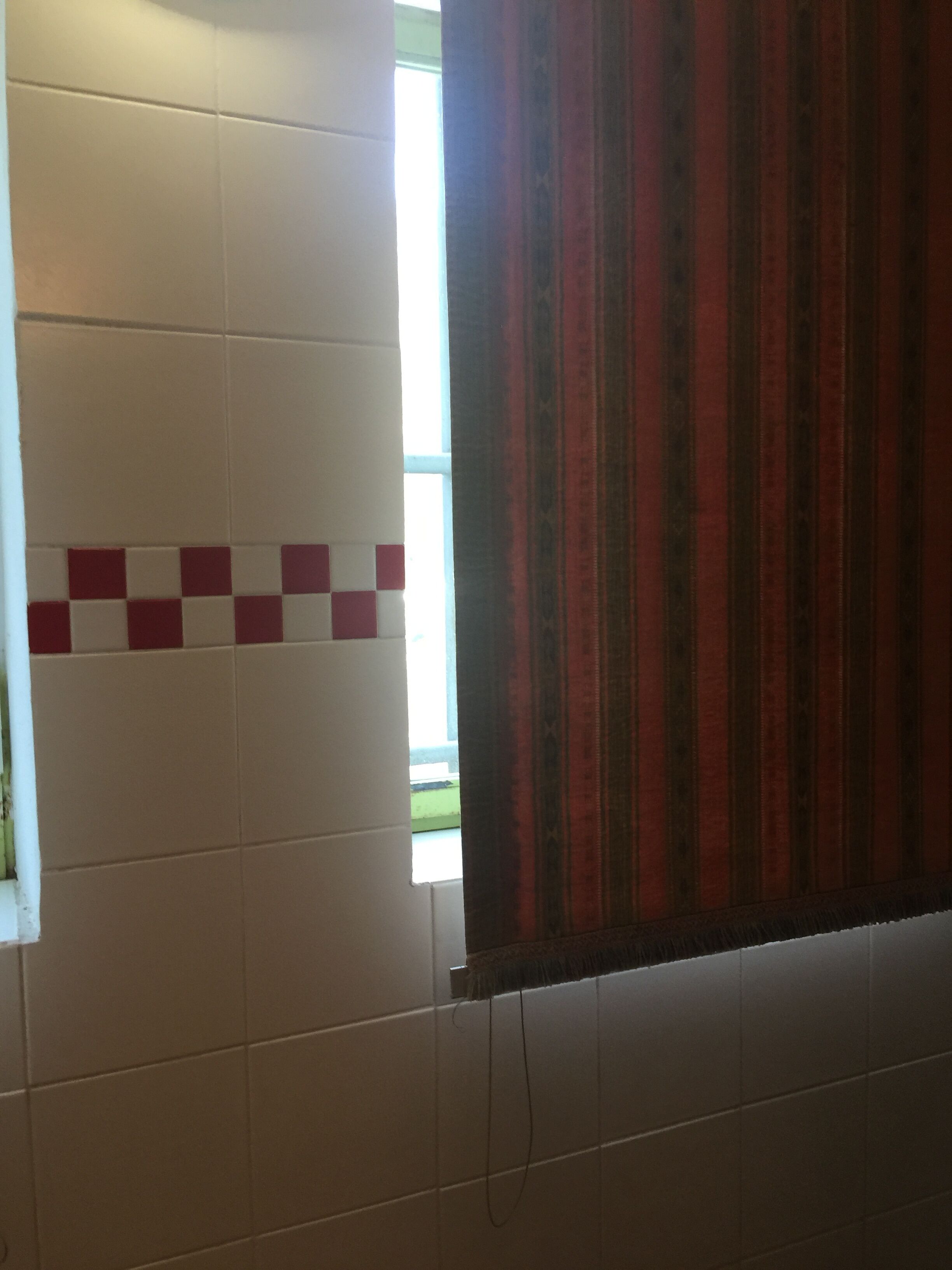 Um banheiro com azulejos brancos e cortina listrada em vermelho e preto.