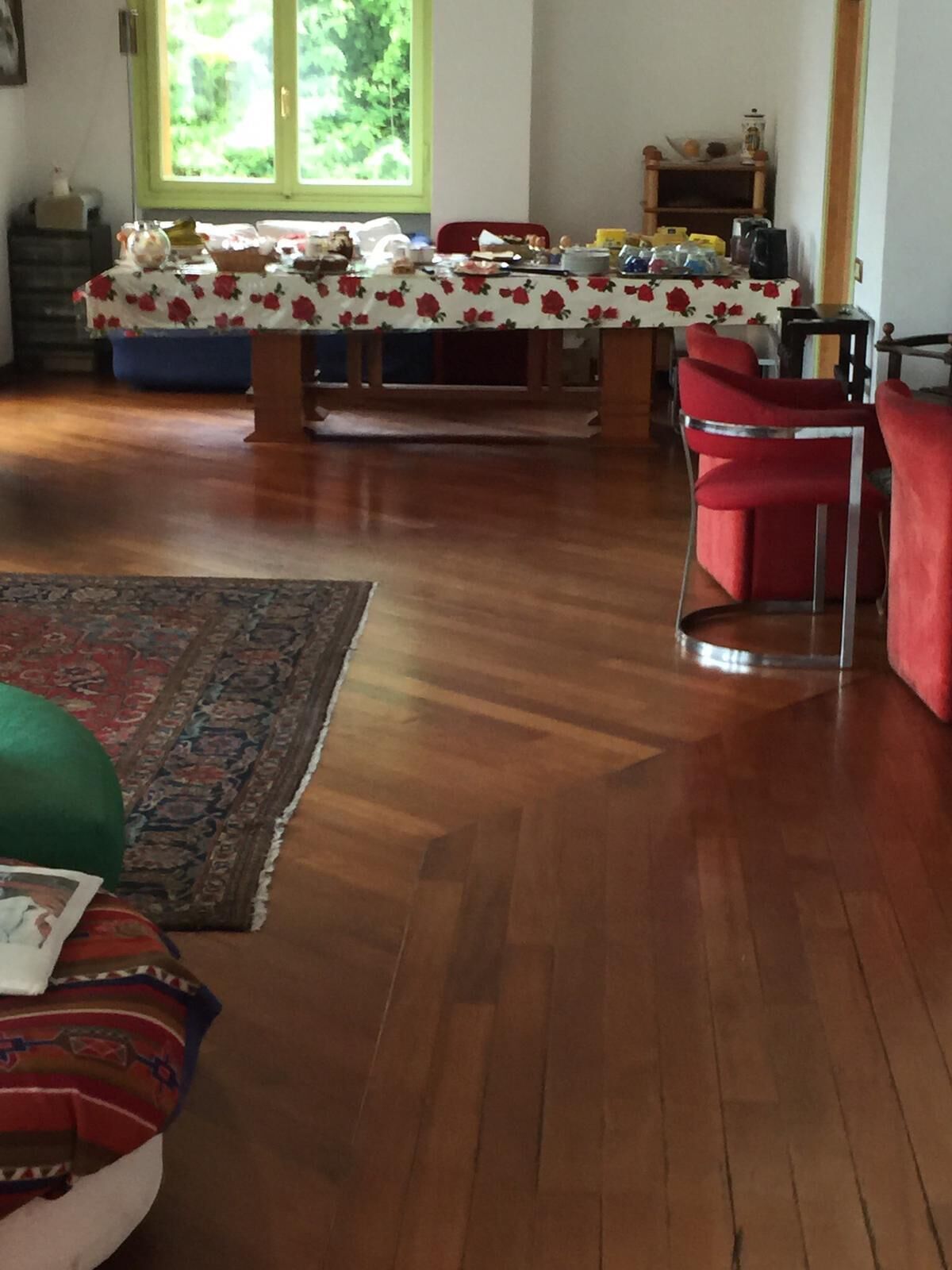 Un coin repas avec une table recouverte d’une nappe à motifs floraux, des chaises rouges et un plancher en bois.