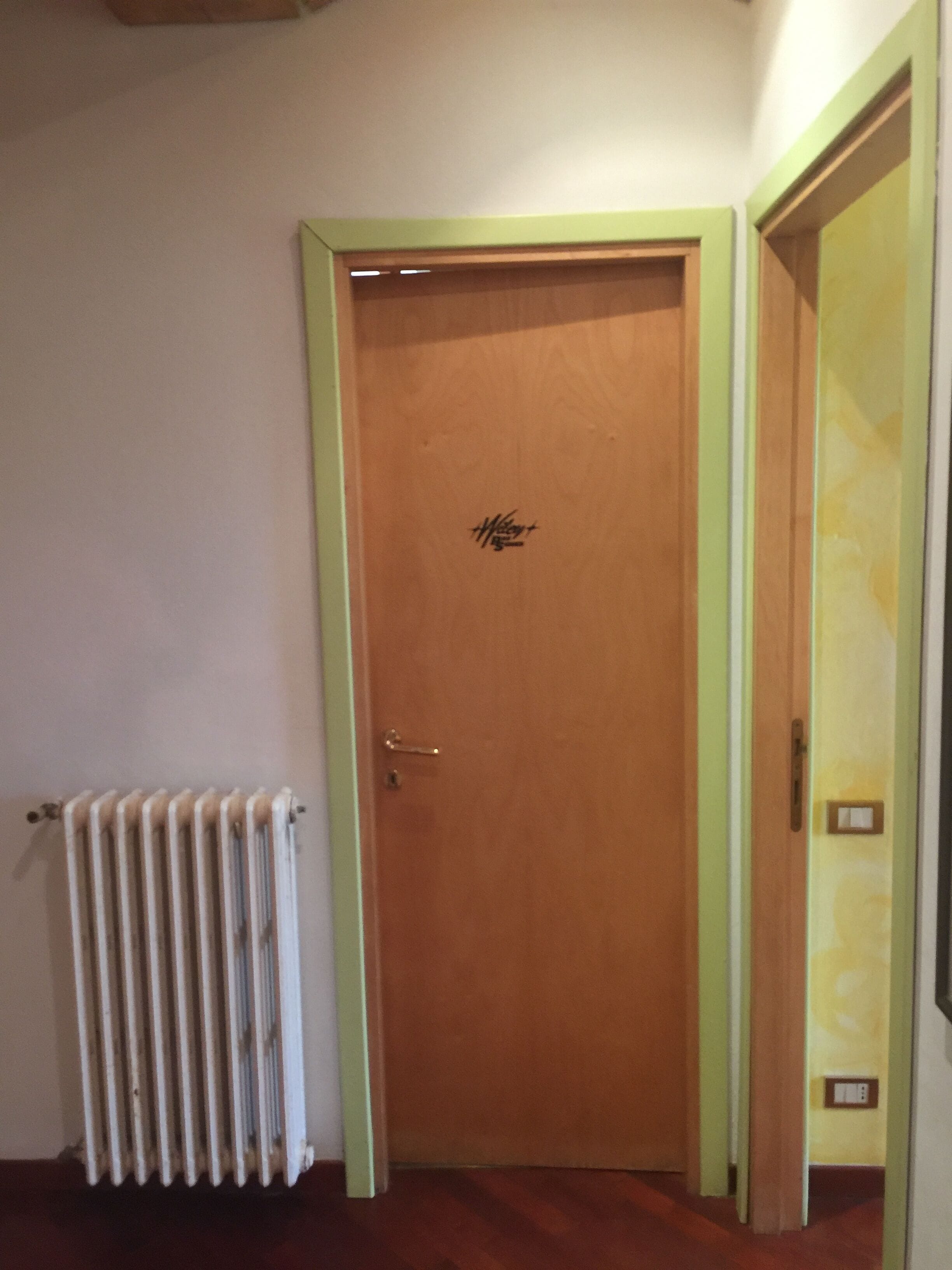 Een houten deur met een groene omlijsting, een radiator links en een effen muur.