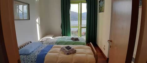 Een hotelkamer met twee bedden en uitzicht op een meer, met een deur aan de linkerzijde.