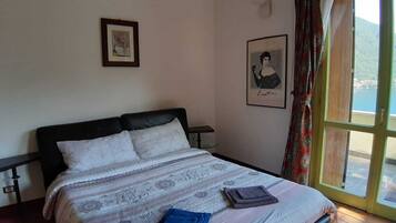A bedroom with a bed, a nightstand, a window with a view of a body of water and hills, and two framed pictures on the wall.