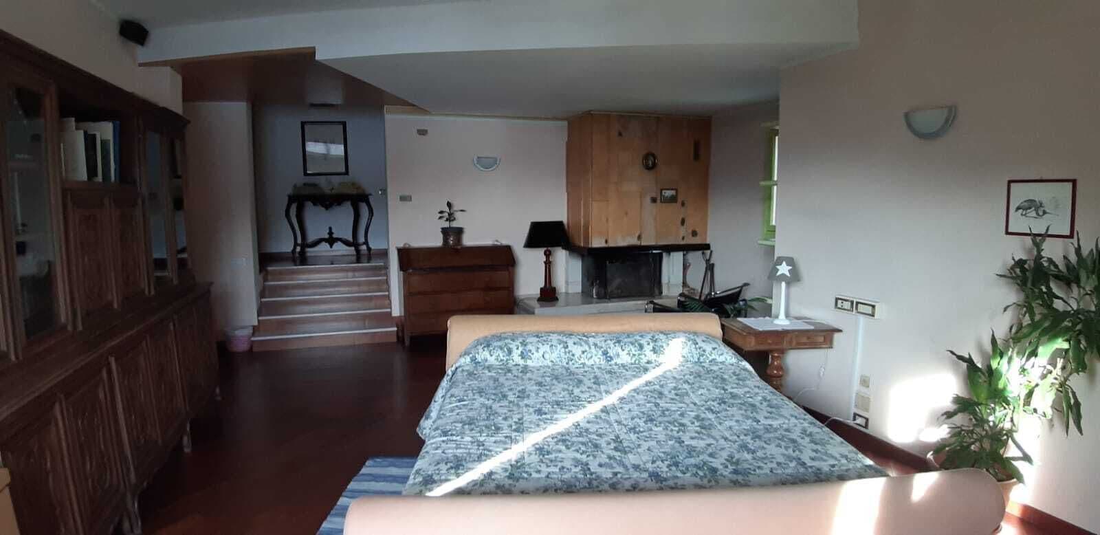 A bedroom with a bed, a wooden cabinet, a desk, a chair, a lamp, a fireplace, and a staircase leading to another room.