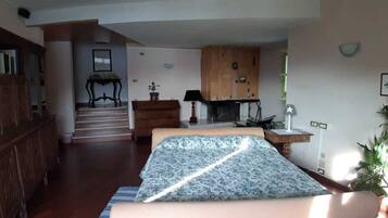 A bedroom with a bed, a wooden cabinet, a desk, a chair, a lamp, a fireplace, and a staircase leading to another room.