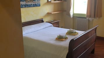 Ein Schlafzimmer mit einem hölzernen Bett, einem Nachttisch, einem Heizkörper, einem Fenster mit Vorhängen und einem Regal mit Büchern und einem gerahmten Bild.